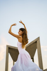 Fototapeta na wymiar Young adult woman wearing a white dress dancing outdoors.