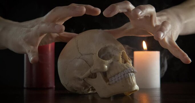 Conjure over the skull. Female hands conjure over a smoking human cherap on a mona of burning candles.