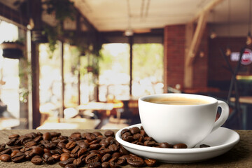Cup of aromatic coffee and beans on wooden table in cafe