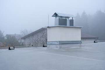 Flat roof covered with bitumen membrane and silver lacquer with chimney on a private house. Cloudy...