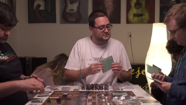 Friends playing board games, sitting around table and thinking before turn, slider view