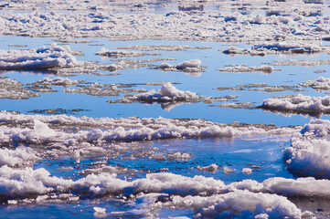 Ice floes float on the river. Seasonal ice drift. Reflection of the blue sky in the water. Natural texture. Selective focus.