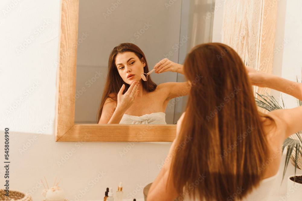 Poster Lovely young woman massages the contour of her face with a jade roller. Beauty and anti-aging procedure for skin care.