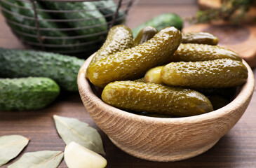 Bowl of pickled cucumbers and ingredients for food preservation on wooden table, closeup