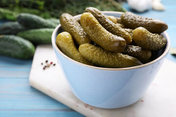 Bowl with pickled cucumbers on light blue table, closeup