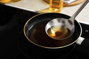 Ladle with used cooking oil over frying pan on stove