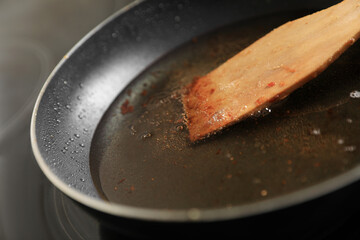Frying pan with spatula and used cooking oil on stove, closeup