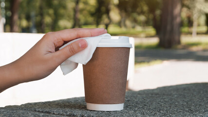 Woman cleaning lid of coffee cup with wet wipe outdoors, closeup. Protective measures