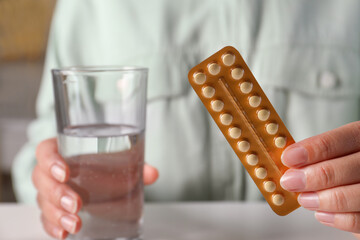 Woman holding blister of oral contraceptive pills and glass with water at white table, closeup - obrazy, fototapety, plakaty