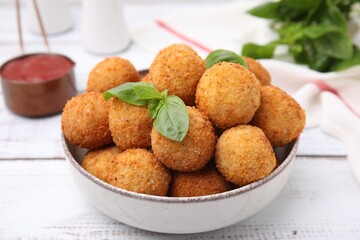 Bowl of delicious fried tofu balls with basil on white wooden table