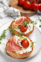 Tasty rusks with prosciutto, cream cheese and tomatoes served on white table, closeup