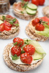 Fototapeta na wymiar Crunchy buckwheat cakes with cream cheese, tomatoes and cucumber slices on white table, closeup