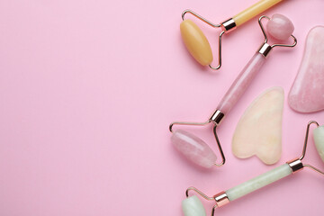 Different gua sha stones and face rollers on pink background, flat lay. Space for text