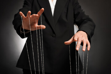 Woman in suit pulling strings of puppet on dark background, closeup
