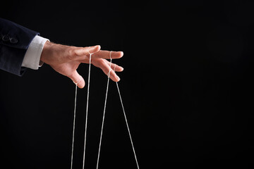 Man pulling strings of puppet on black background, closeup. Space for text