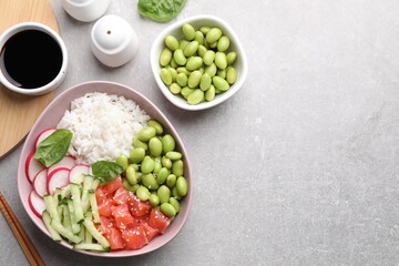 Poke bowl with salmon, edamame beans and vegetables on light grey table, flat lay. Space for text