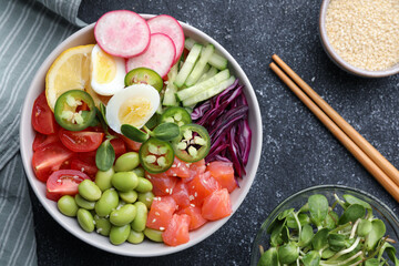 Poke bowl with salmon, edamame beans and vegetables on black table, flat lay