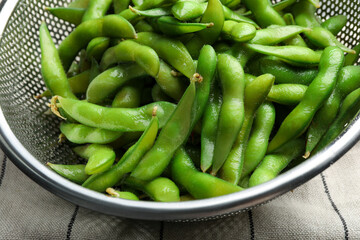 Sieve with green edamame beans in pods on table, closeup