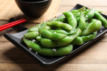 Black plate with green edamame beans in pods on wooden table