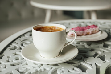 Cup of delicious aromatic coffee and eclair on table indoors