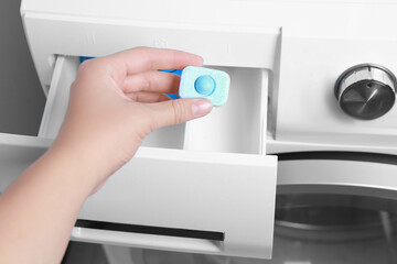 Woman putting water softener tablet into washing machine, closeup