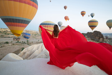 a girl in a flying dress with a long train on the background of balloons in Cappadocia.