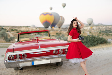 beautiful girl retro style posing near vintage red cabriolet car with old film camera  on...