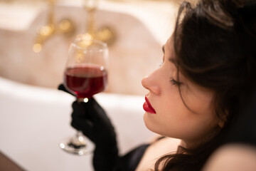 beautiful girl in erotic lingerie sitting in the bathroom with a glass of wine.