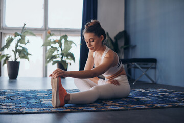 Confident young woman doing stretching exercises while sitting on the carpet at home