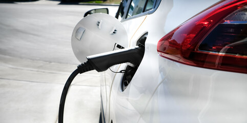 Electric car concept with charger . White vehicle with black charger is charging at home. Zero...