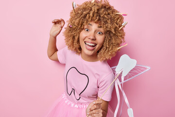 Positive female dental fairy dances carefree with magic wand smiles broadly dressed in t shirt and skirt comes on costume party entertains children smiles broadly isolated over pink background