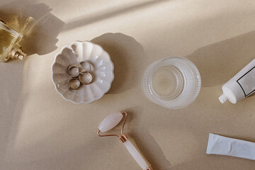 Woman's tools and accessories on the beige table. Cosmetics, jade roller, water, rings