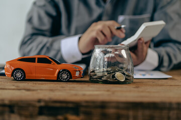 Fototapeta na wymiar Piggy bank and toy car house on the table with man as background, money saving concept for paying for the car, house.