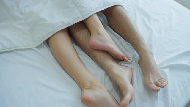 Close up feet of young couple starting foreplay and making love on bed. 