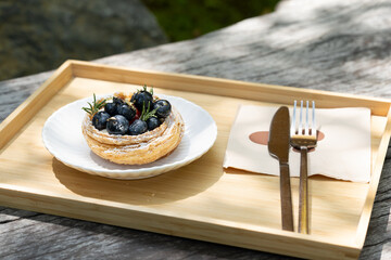 Blueberry tart with knife and fork on wooden tray in natural light.