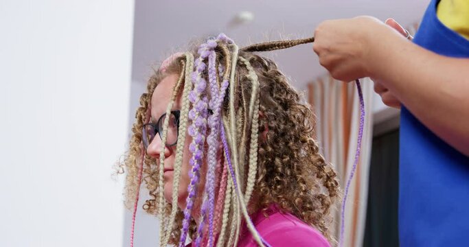 Woman customer undergoes process of removing fake dreads in beauty salon. Professional hairdresser untangles dreadlocks with scissors. Customer enjoys relax