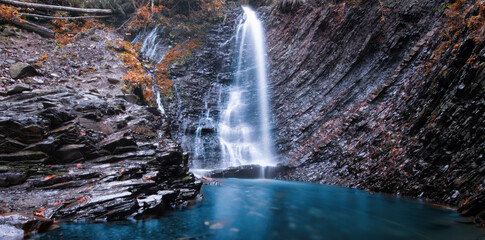 Fototapeta na wymiar Mountain waterfall. Precipitous stone rock, grass and trees. A wonderful mountain landscape.