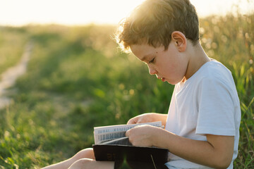 Christian boy holds bible in her hands. Reading the Holy Bible in a field during beautiful sunset....