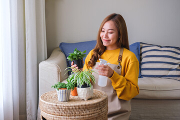 Portrait image of a beautiful young woman taking care and watering houseplants with plant mister spray at home