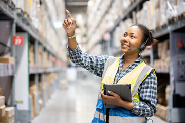 Portrait of young attractive African American woman auditor or trainee staff work looking up stocktaking inventory in warehouse store by computer tablet and headphones near products shelf. Call center