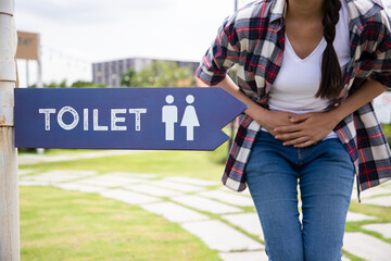 Bowel incontinence pain. Woman hand holding crotch near sign toilet in the park. Finding location for ease