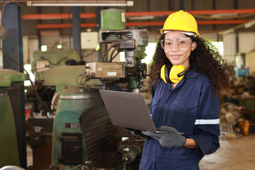 Technician engineer woman in protective uniform working with computer while maintenance operation or checking lathe metal machine at heavy industry manufacturing factory. Metalworking concept