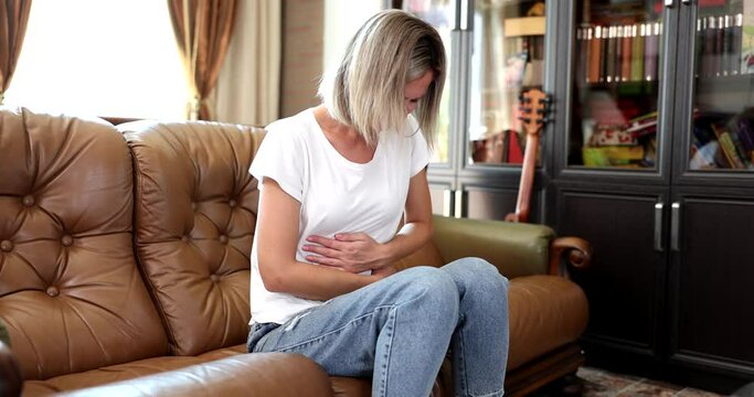 sad woman sits on couch at home, suffering after miscarriage or abortion