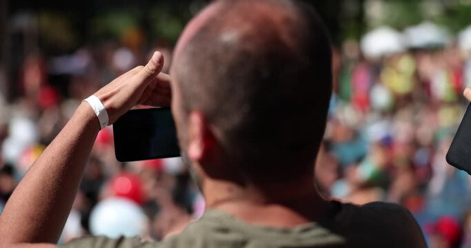 Man lifted his cell phone camera to film rally crowd of people or rear view concert