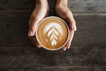 Latte art coffee with heart tree  shape in coffee cup holding by hand on wooden background, Hot...