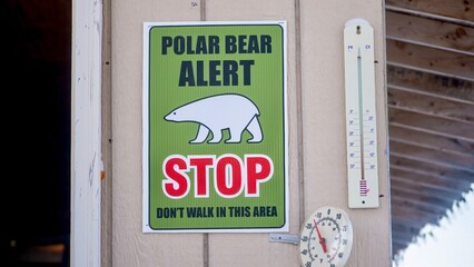 A polar bear alert sign and two outdoor thermometers showing sub zero temperatures, attached to an exterior house wall in northern Canada.