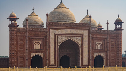 The ancient red sandstone mosque of the Taj Mahal complex. Decorated with white marble and inlays. Domes, towers, arched entrances are visible. Blue sky. India. Agra