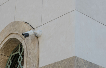 Closed circuit TV camera beside window frame of marble walled building.