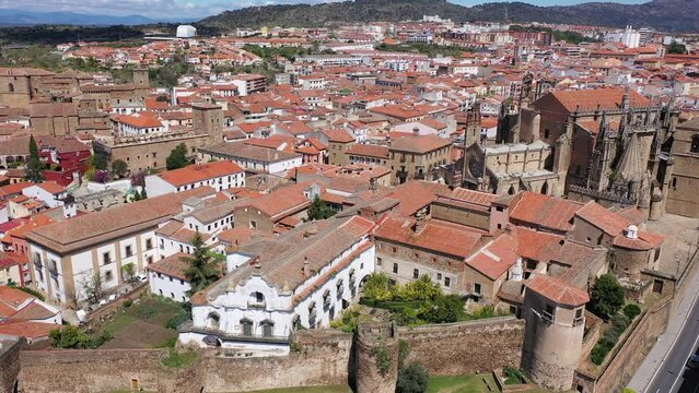 Drone view of picturesque cityscape of historical part of Placencia surrounded by ancient fortress wall overlooking tiled roofs of houses and medieval gothic cathedral on sunny spring day, Spain. High