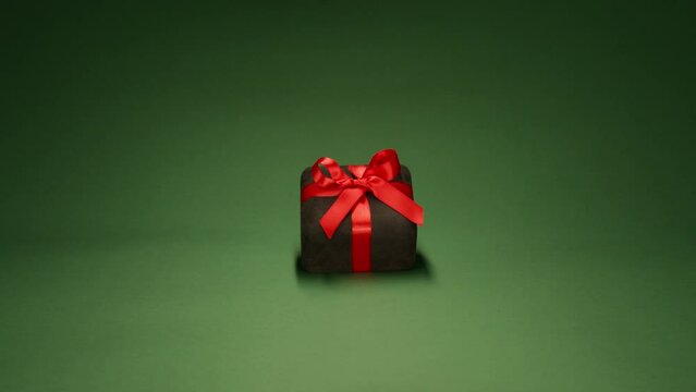 Copy space background for love and birthday surprise engagement concept footage. Cinematic dolly shot of velvet black gift box, scarlet red satin ribbon with elegant bow on Christmas green background